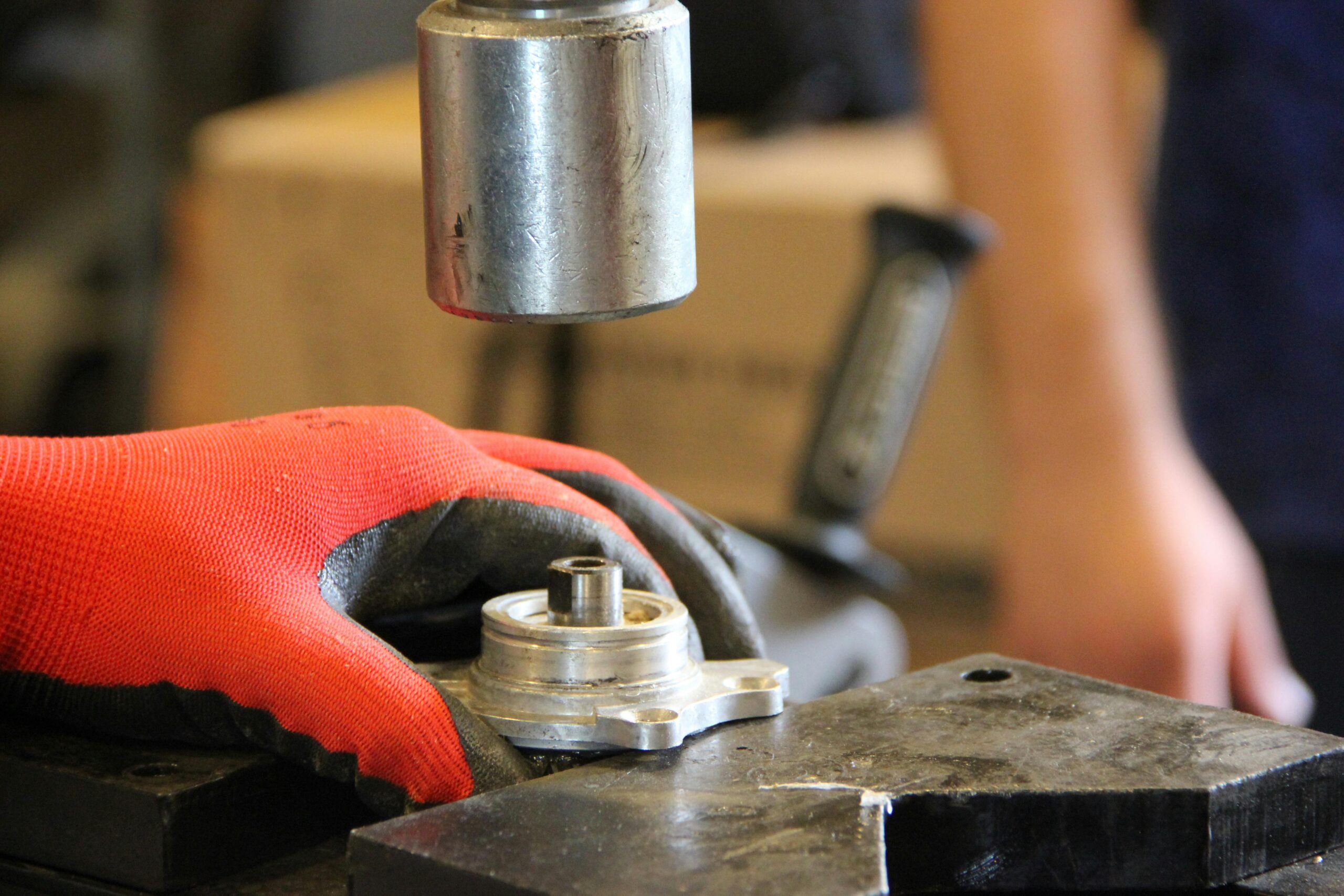 Hands in red gloves operate metal machinery in workshop close-up.